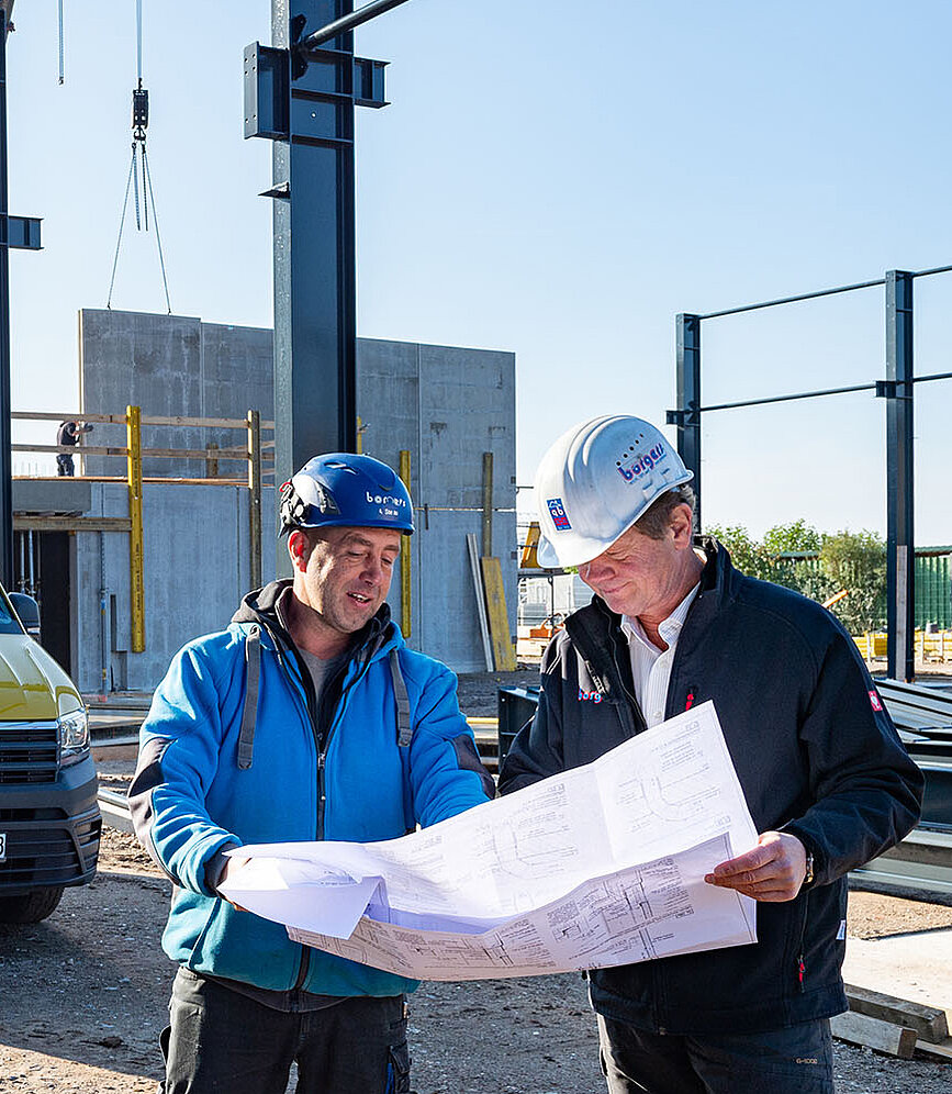 Zwei Mitarbeiter blicken auf der Baustelle auf einen Plan