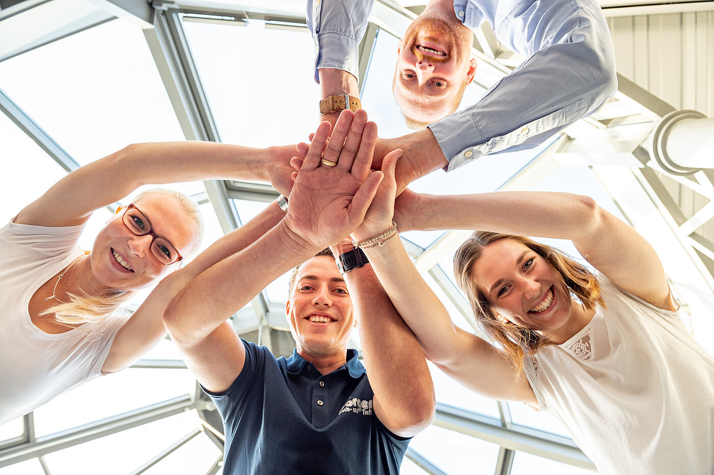 Vier Mitarbeitende stehen im Kreis und legen die Hände übereinander